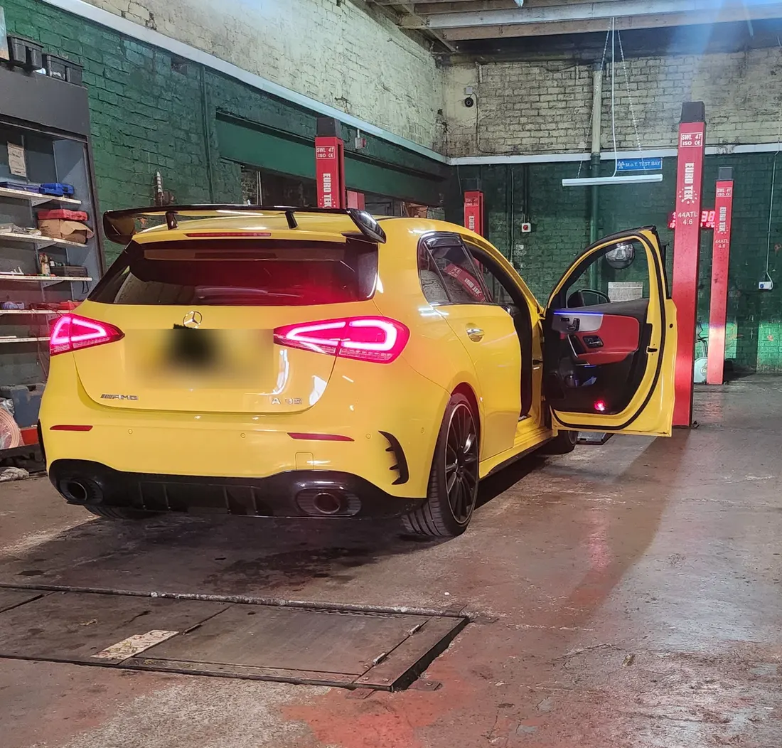 A yellow Mercedes hatchback with its door open in the workshop
