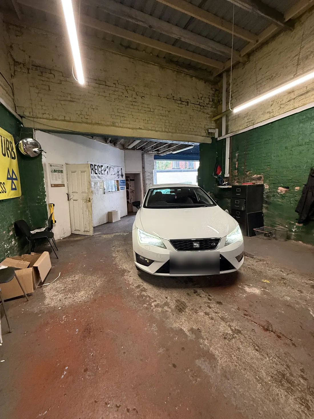 Inside: a long hall with green-painted brick walls, strip lights and a white hatchback in the middle of the floor