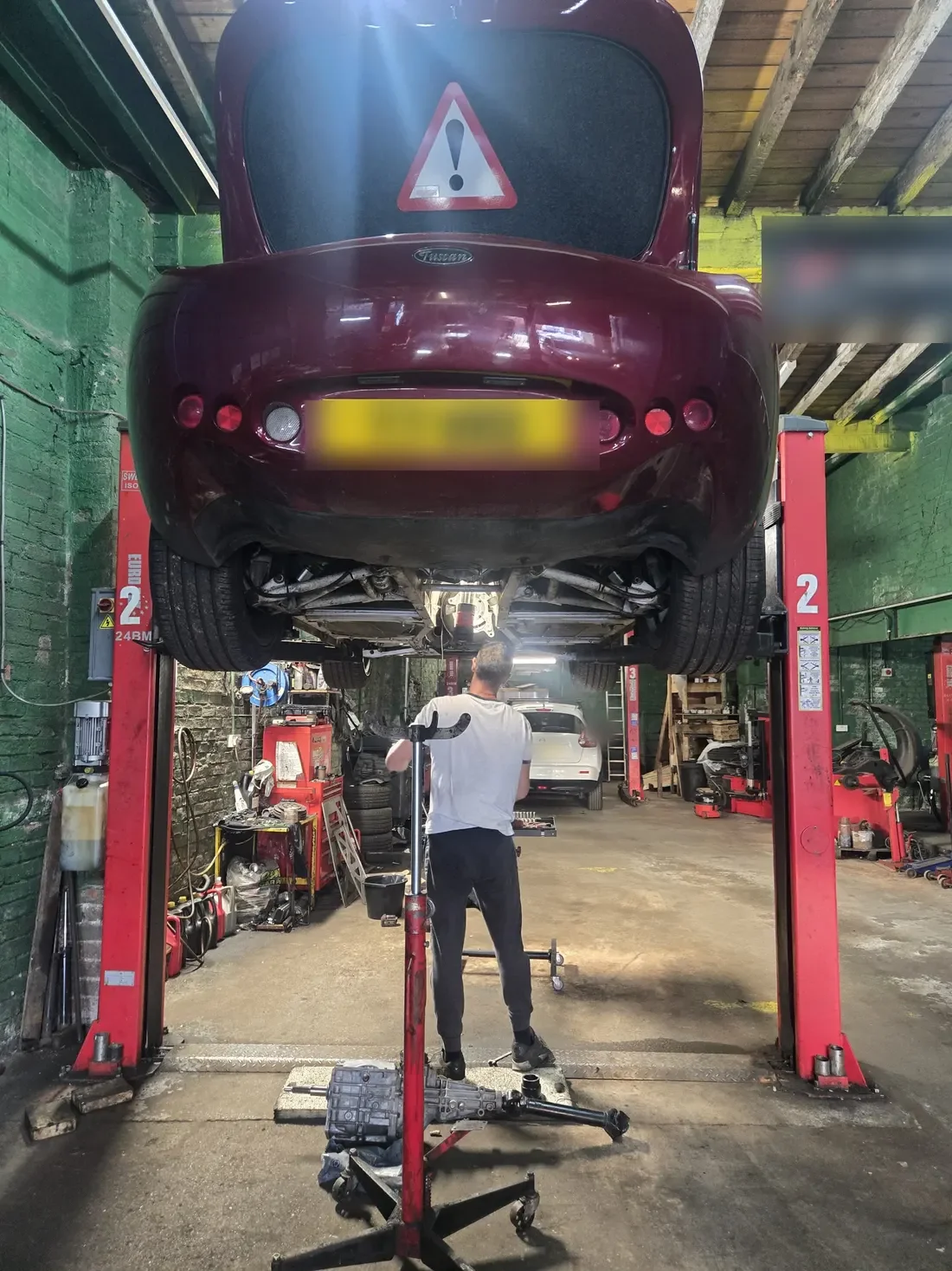 A red TVR raised on a two-post lift, seen from underneath