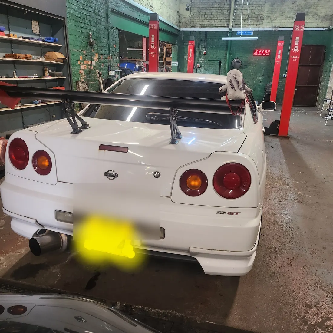 A white Nissan Skyline with a rear wing, parked in front of the red lift posts