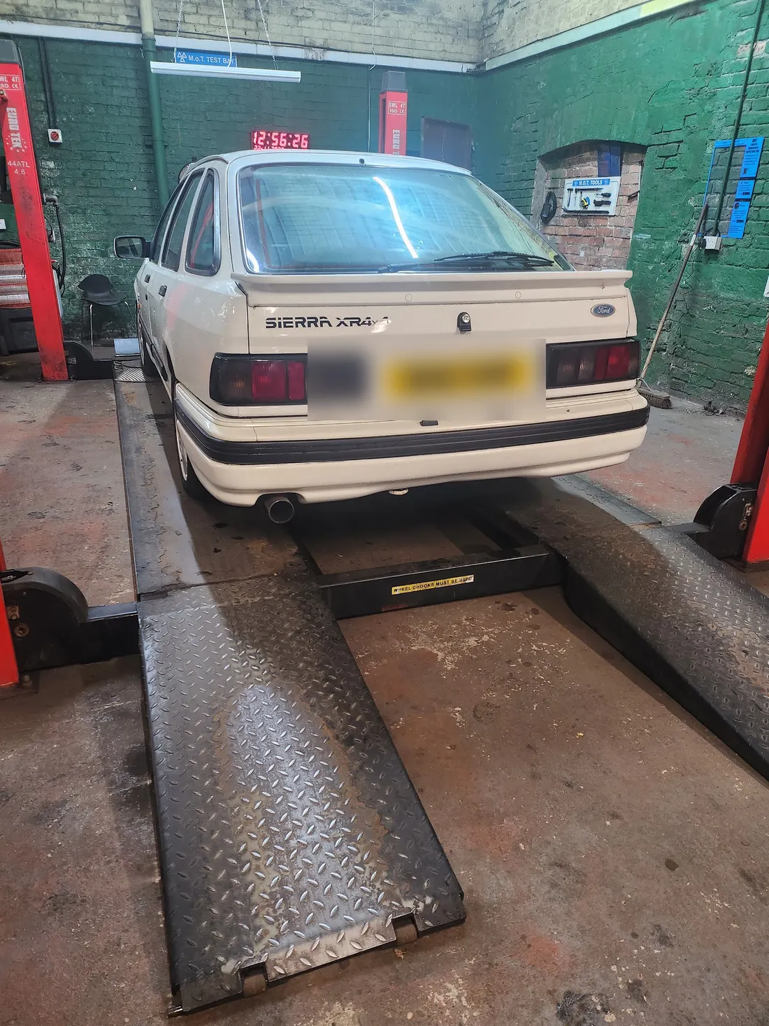 A white Ford Sierra on the inspection ramp rails, seen from behind